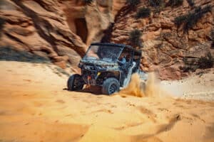A UTV driving in red sand near a slot canyon
