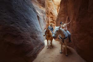 23 Zion Adventures for 2023 18 two people riding horses in a slot canyon