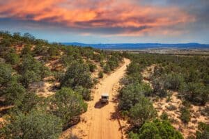 A jeep driving over red rock into the sunset